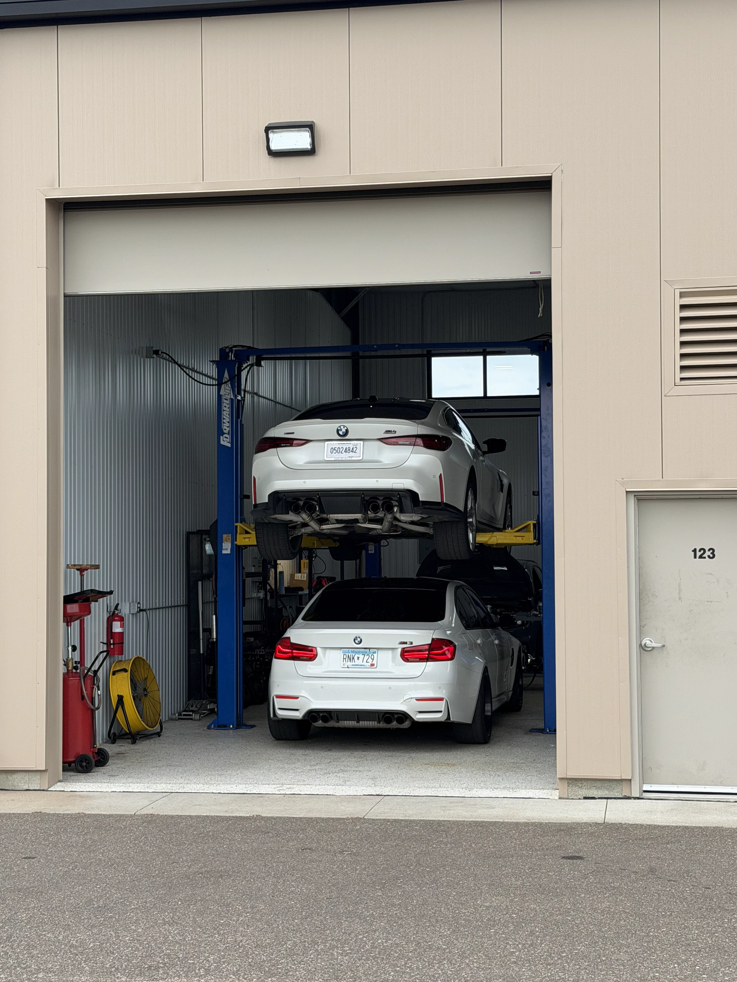 Bay door 123 with two white BMWs in the shop