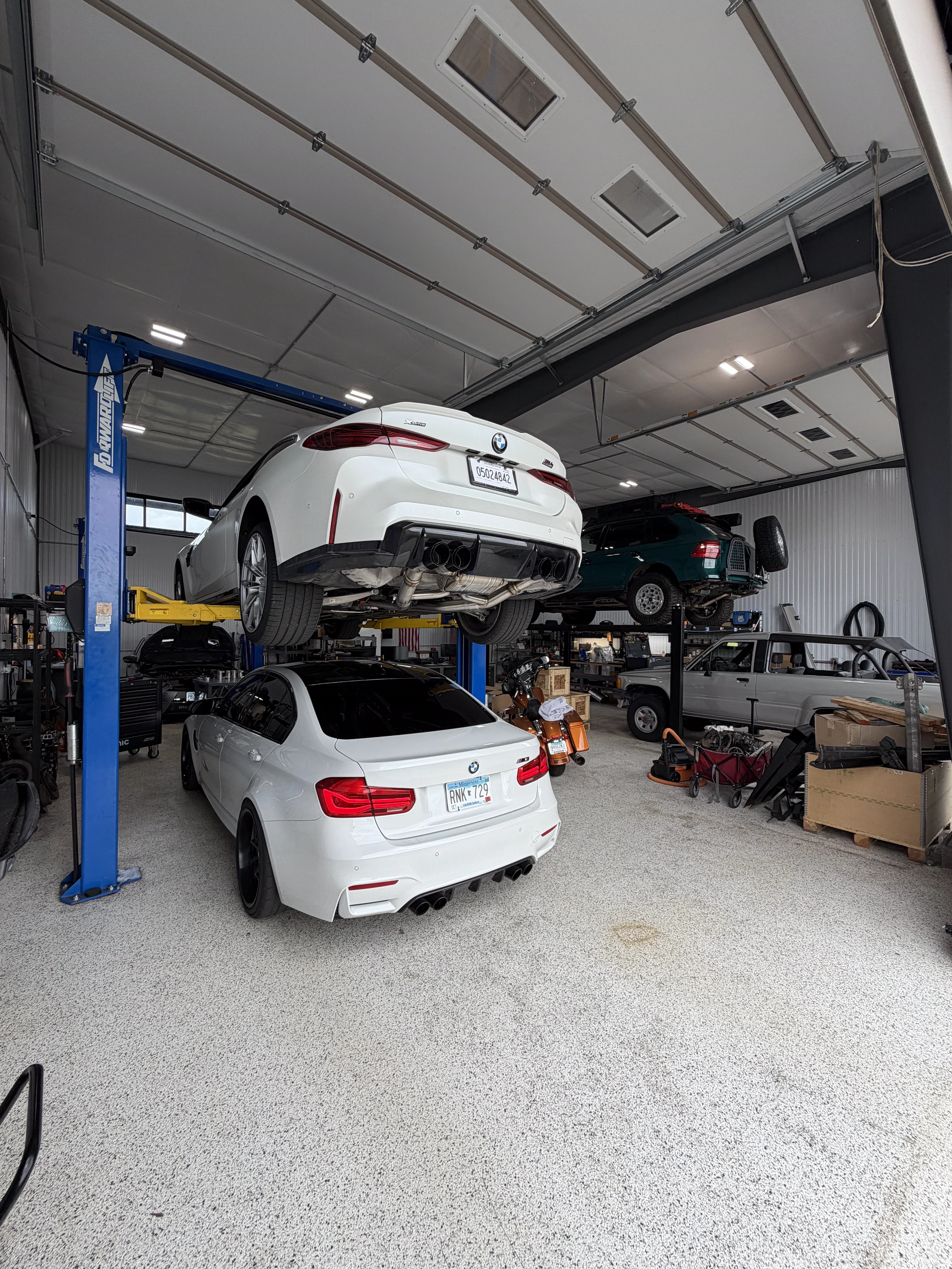 White BMW M4 on the lift and a BMW M3 below it during shop work